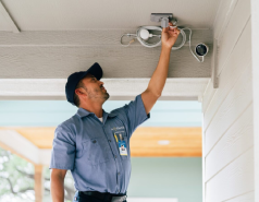 Male Mr. Electric associate inspecting electrical outlet and light bulb outside residential home.