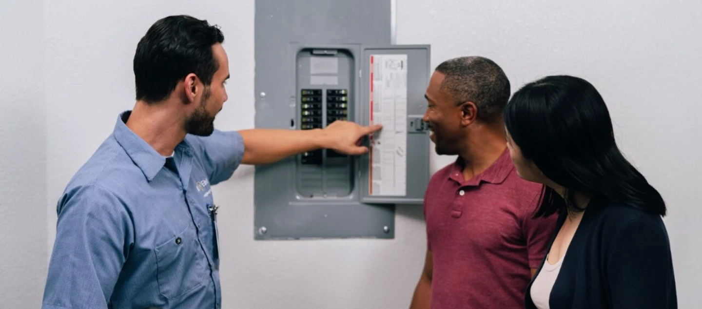 Mr. Electric electrician showing a circuit breaker board to two people during an electrical panel upgrade appointment