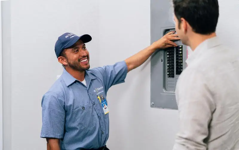 A Mr. Electric electrician talking to a customer in front of the circuit breaker.