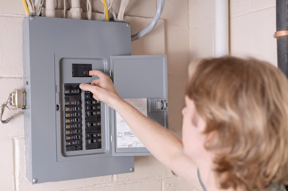 A Mr. Electric professional flipping the main breaker in an electrical panel